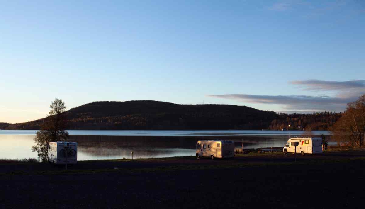 Camper am ruhigen See in der Dämmerung, mit dunkler Hügelsilhouette und klarem Abendhimmel.