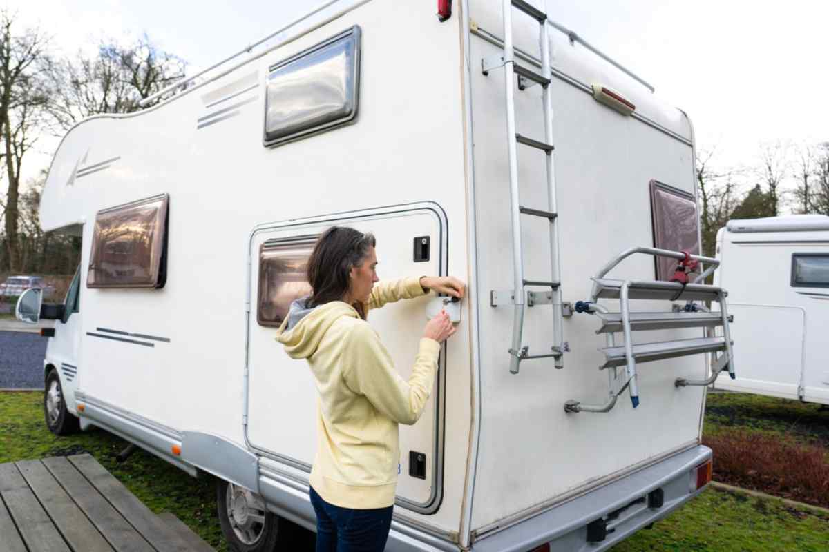 Frau prüft eine Außenklappe am camper auf einem Campingplatz, in der Nähe steht ein weiteres wohnmobil.